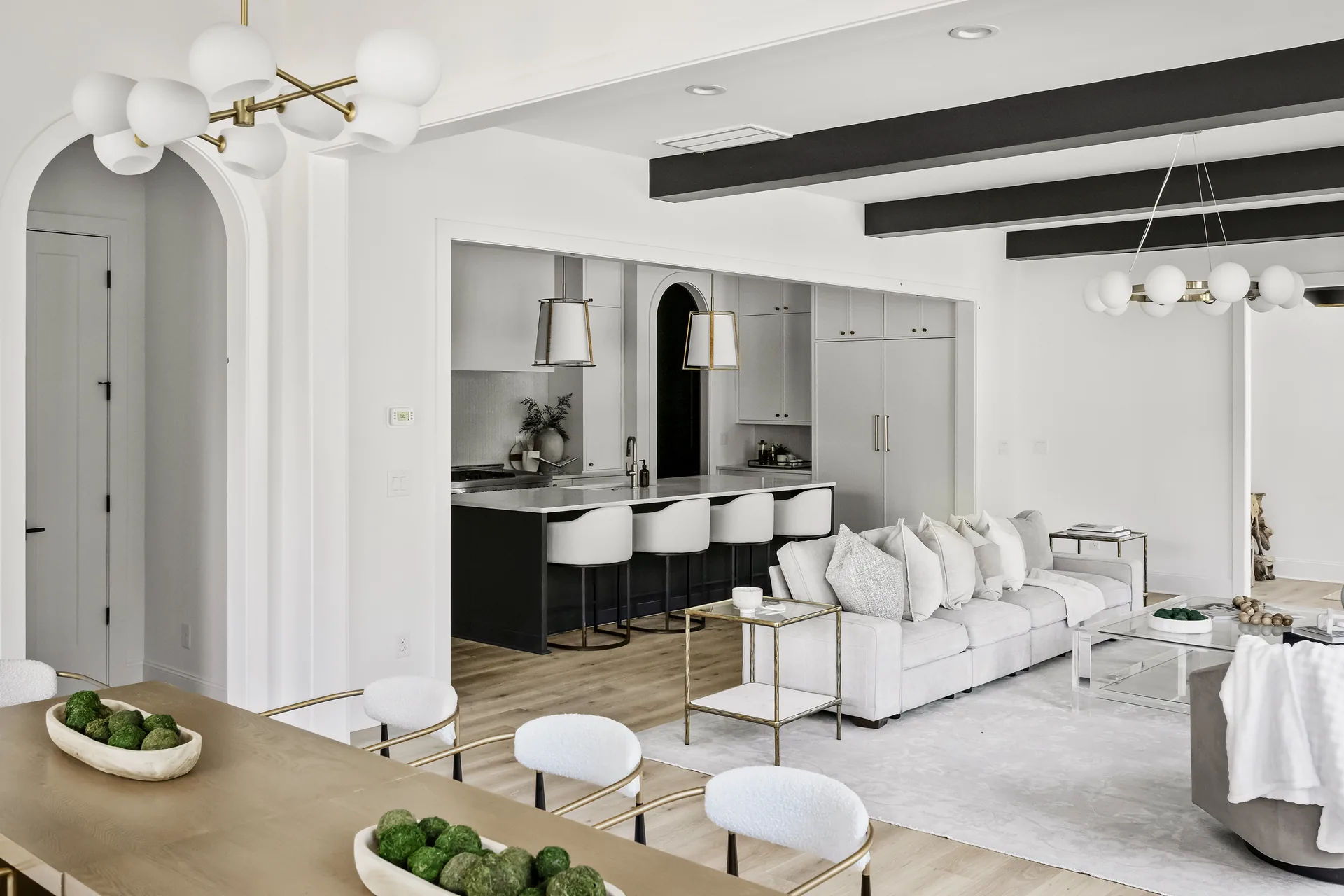 Open-plan dining, kitchen, and living room with black beams and warm brass lighting.